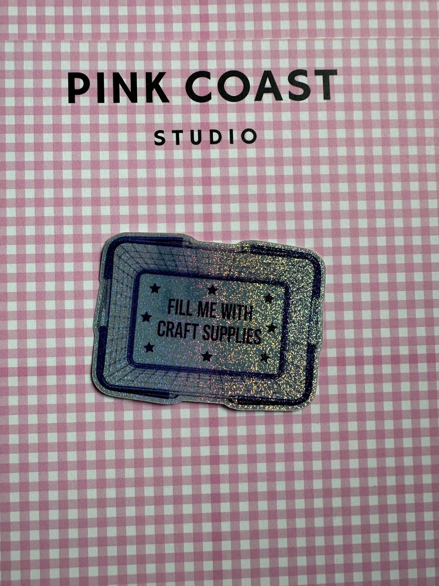 Glitter sticker with text on a pink and white checkered background, featuring 'Pink Coast Studio'.