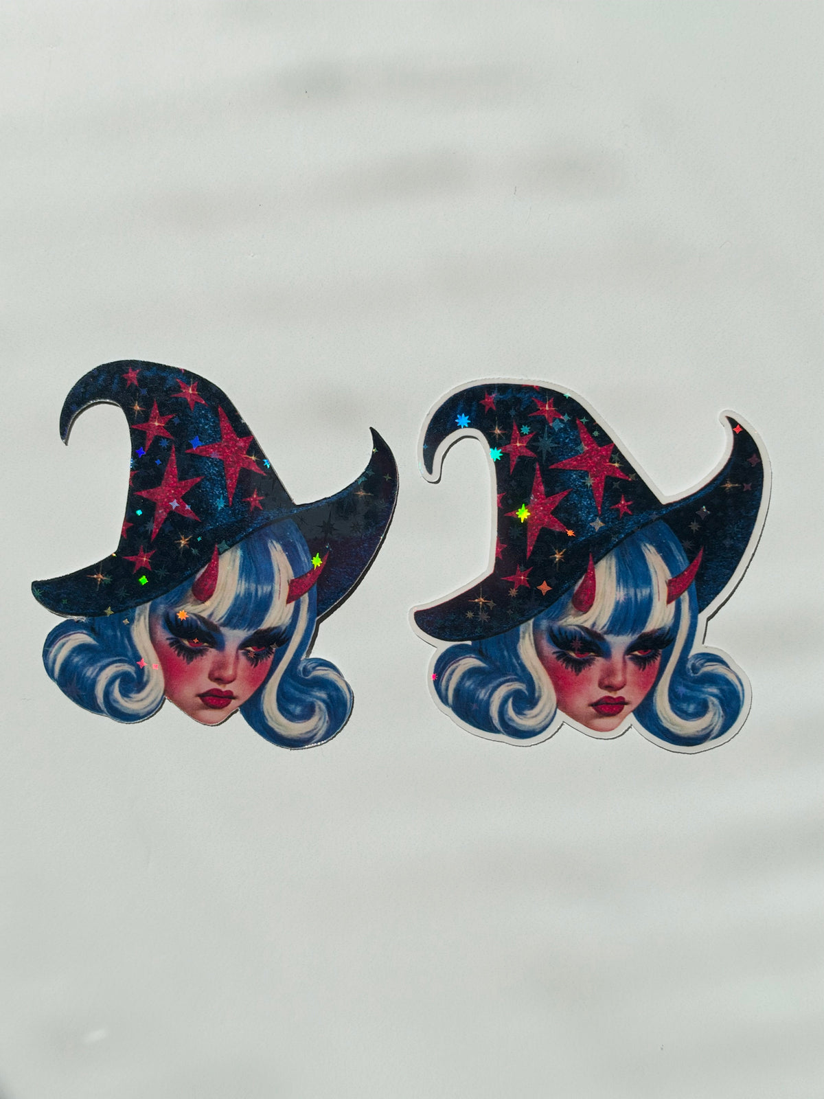 Two identical witch hat stickers with holographic star details, featuring a stylized face with blue hair, displayed on a light gray background.