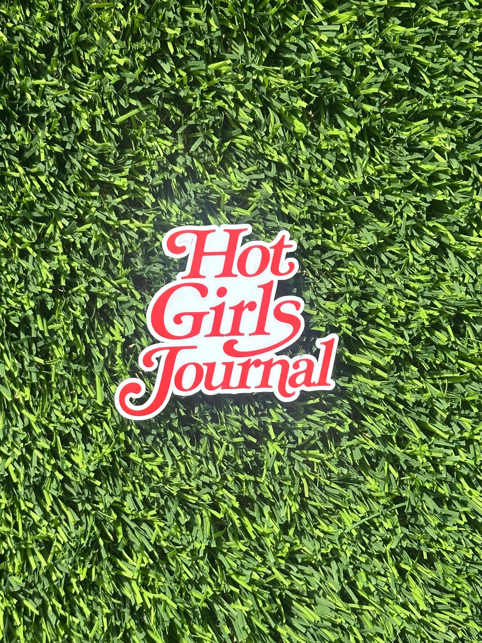 Sticker with 'Hot Girls Journal' text on artificial grass background