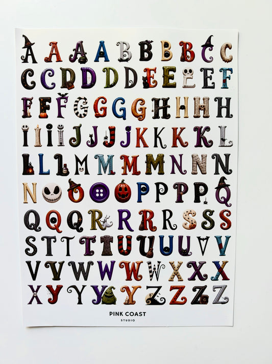 A printed alphabet sticker sheet featuring decorative, illustrated letters arranged in rows on a white sheet, with the text 'PINK COAST STUDIO' at the bottom, photographed against a light neutral background.
