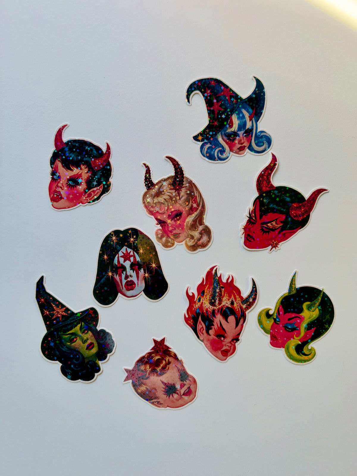 A set of nine colorful devil and witch mask stickers arranged on a plain white background.